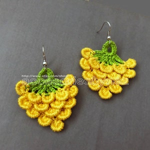 May include: A pair of crocheted earrings shaped like bunches of grapes. The earrings are yellow and green and have a silver hook.