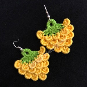May include: A pair of crocheted earrings shaped like bunches of grapes. The earrings are yellow and green and have silver hooks.