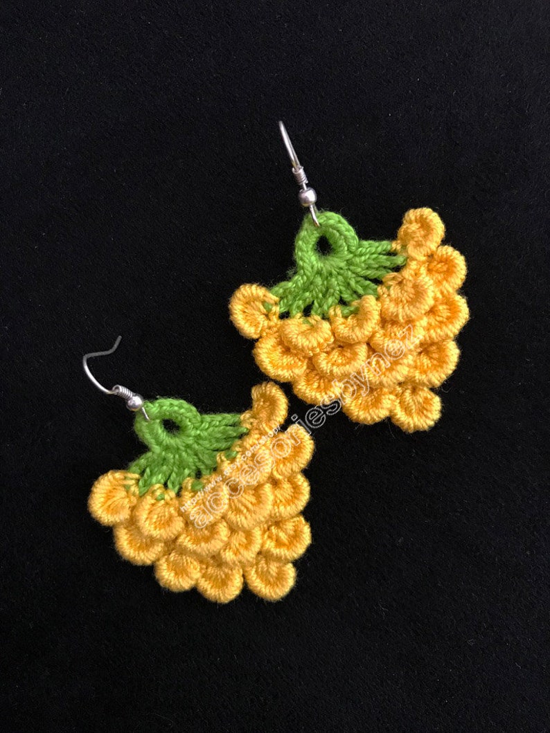 May include: A pair of crocheted earrings shaped like bunches of grapes. The earrings are yellow and green and have silver hooks.