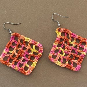 May include: A pair of crocheted earrings with a geometric design in shades of orange, pink, and yellow.