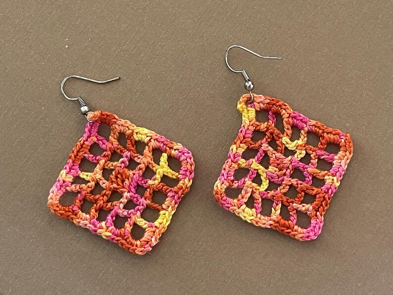 May include: A pair of crocheted earrings with a geometric design in shades of orange, pink, and yellow.