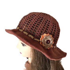 May include: A brown crocheted sun hat with a flower embellishment. The hat has a wide brim and a crocheted design.