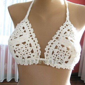 May include: White crocheted bikini top with a delicate floral pattern. The top has adjustable straps and a halter neck style.