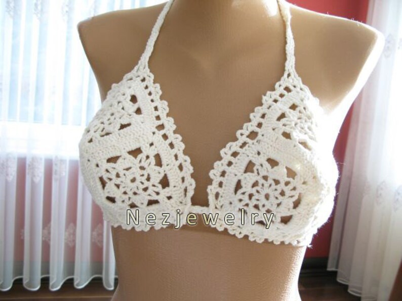 May include: White crocheted bikini top with a delicate floral pattern. The top has adjustable straps and a halter neck style.