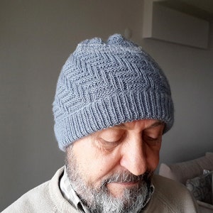 Puede incluir: Un gorro de punto gris con un patr&oacute;n texturizado. El gorro lo lleva puesto una persona con barba.