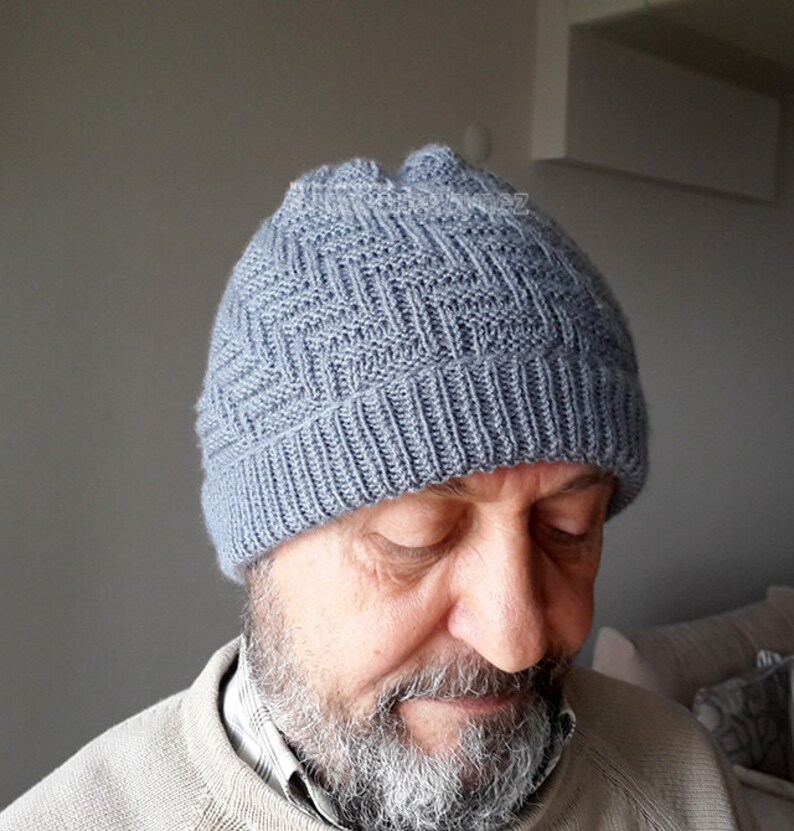 Puede incluir: Un gorro de punto gris con un patr&oacute;n texturizado. El gorro lo lleva puesto una persona con barba.