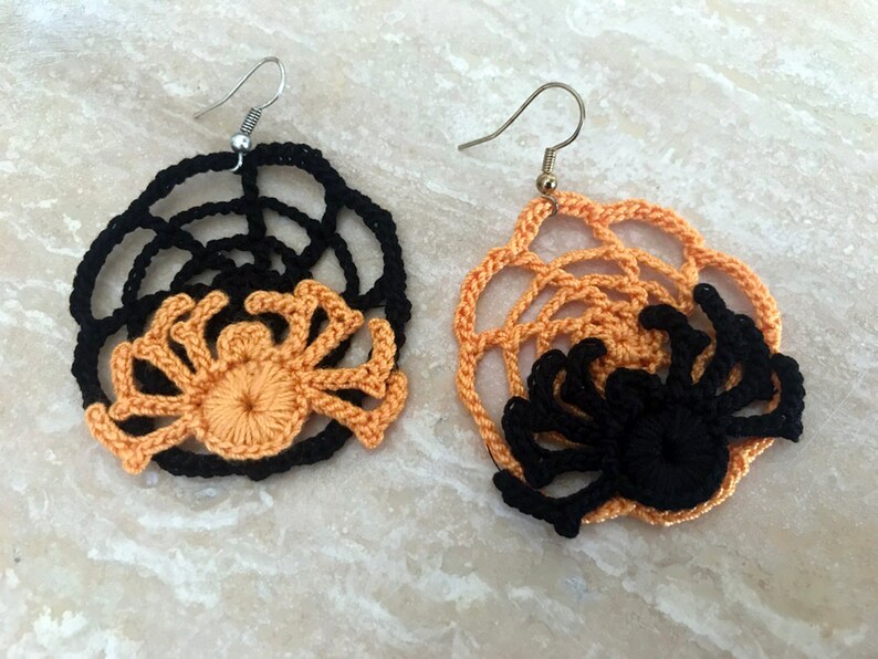 May include: A pair of crocheted spider earrings with black and orange webs. The earrings are made with a black web and a crocheted orange spider in the center.