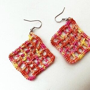 May include: A pair of crocheted earrings with a geometric design in shades of pink, orange, and yellow.