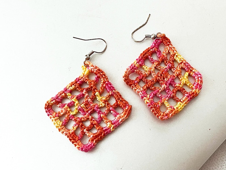 May include: A pair of crocheted earrings with a geometric design in shades of pink, orange, and yellow.