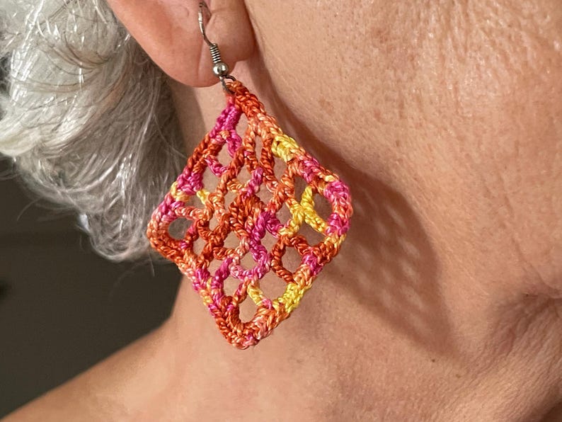 May include: A pair of crocheted earrings in a diamond shape. The earrings are made with orange, pink, and yellow yarn.
