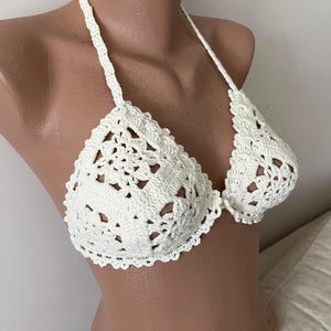 May include: White crochet bikini top with a delicate floral pattern. The top has adjustable straps and a halter neck style.