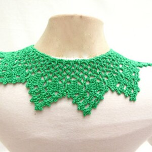 May include: A green crocheted collar necklace. The collar is made of delicate, openwork stitches and has a scalloped edge.