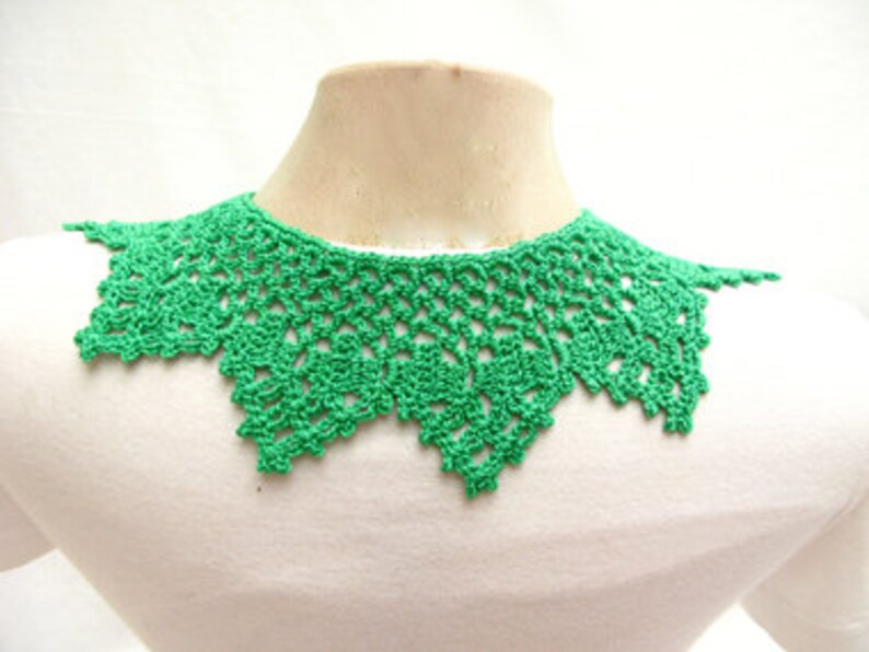 May include: A green crocheted collar necklace. The collar is made of delicate, openwork stitches and has a scalloped edge.