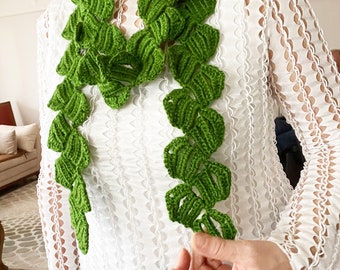 May include: A green crocheted scarf with a leaf design. The scarf is made of yarn and is a handmade item.