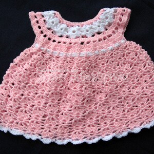 May include: A pink crocheted baby dress with white trim. The dress has a scalloped hem and a white crocheted collar.
