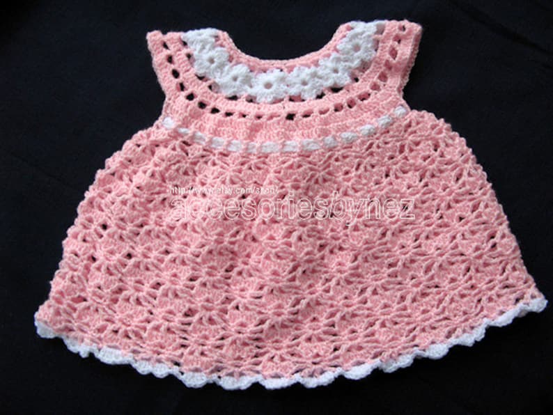 May include: A pink crocheted baby dress with white trim. The dress has a scalloped hem and a white crocheted collar.