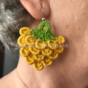 May include: Crocheted earrings with a cluster of yellow flower-shaped embellishments and a green leaf at the top.