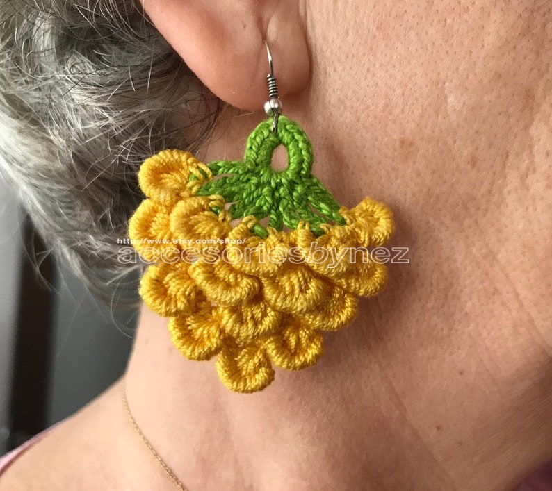 May include: Crocheted earrings with a cluster of yellow flower-shaped embellishments and a green leaf at the top.