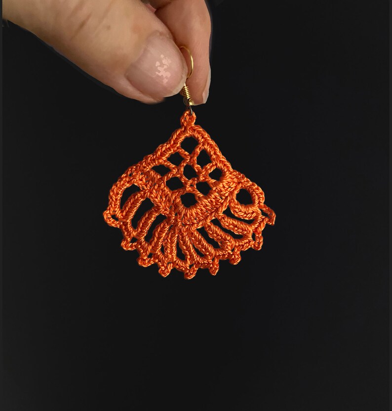 Puede incluir: Pendiente de ganchillo naranja con un delicado dise&ntilde;o floral y un gancho dorado.