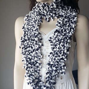 May include: A white and black fuzzy scarf with a chunky knit texture. The scarf is worn by a mannequin with long brown hair.