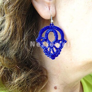 May include: A pair of blue crocheted earrings in the shape of a skull. The earrings are hanging from silver hooks.