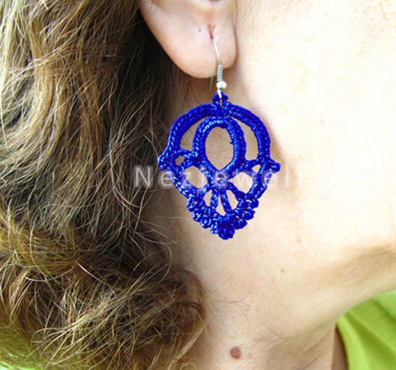 May include: A pair of blue crocheted earrings in the shape of a skull. The earrings are hanging from silver hooks.