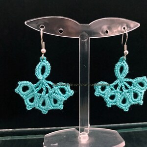 Può includere: Orecchini in crochet color turchese con ganci argentati. Gli orecchini hanno la forma di un ventaglio con un design delicato.