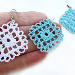 May include: A pair of crocheted earrings, one white and one light blue, with a square shape and intricate designs.