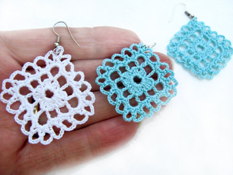 May include: A pair of crocheted earrings, one white and one light blue, with a square shape and intricate designs.