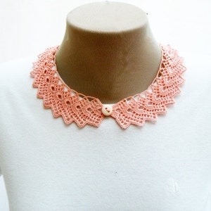 May include: A white t-shirt with a peach-colored crocheted collar. The collar has a button in the center.