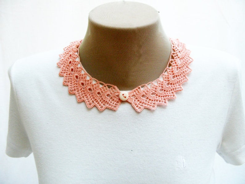 May include: A white t-shirt with a peach-colored crocheted collar. The collar has a button in the center.