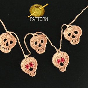 May include: A garland of crocheted pink skull ornaments with red bead accents. The garland is strung together with white yarn. The word "PATTERN" is written in black text on a white background.