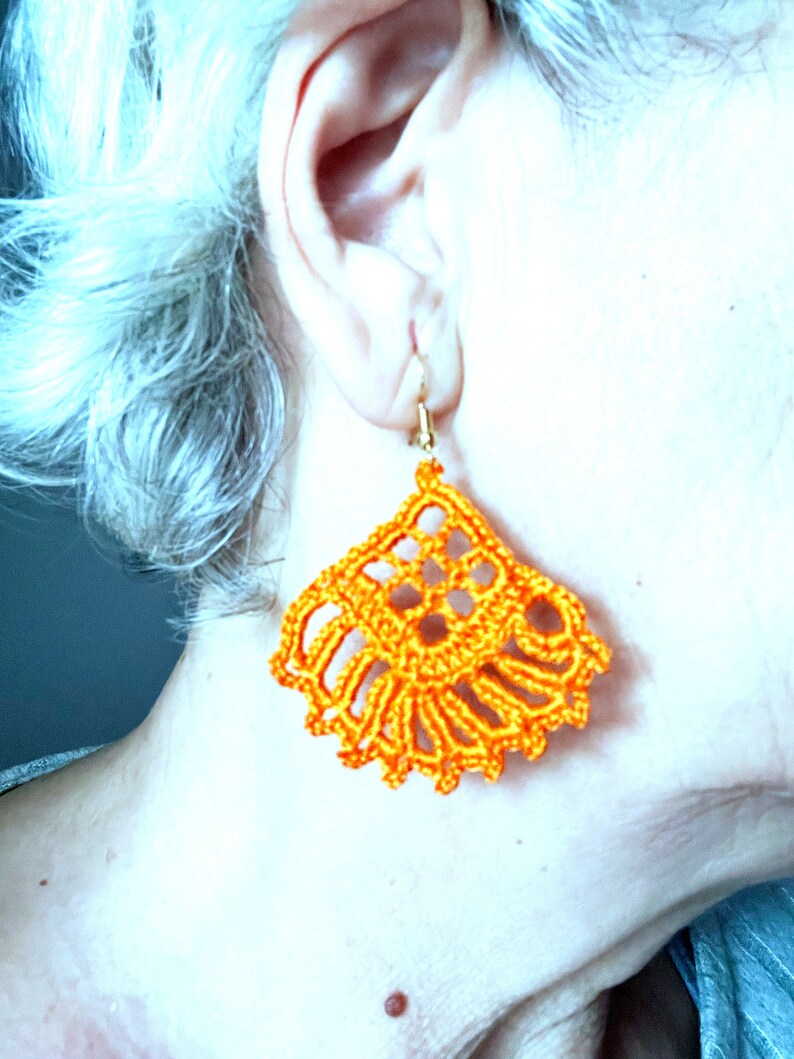 Puede incluir: Pendientes de ganchillo de color naranja con un dise&ntilde;o delicado e intrincado. Los pendientes cuelgan de la oreja de una persona.