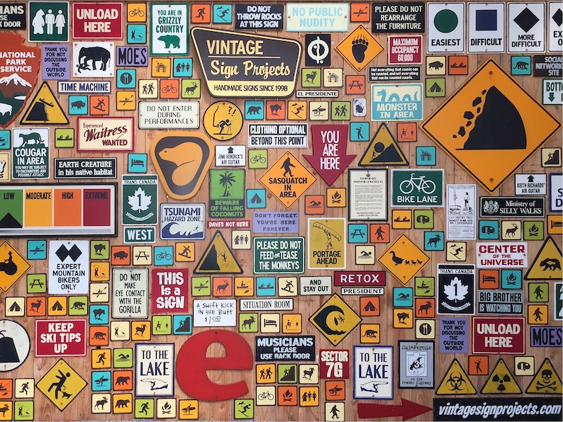 May include: A wall covered in vintage-style metal signs with various warnings, instructions, and humorous messages. The signs are in different shapes, sizes, and colors, with some featuring illustrations. The signs are arranged in a random pattern, creating a visually interesting and eclectic display.