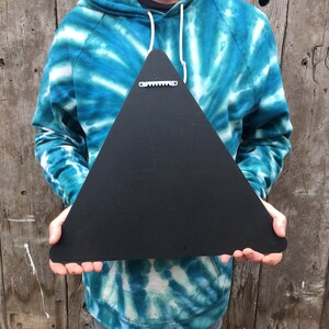 May include: A black, triangular wooden sign with a sawtooth hanger on the back. The sign is held up against a wooden background. The sign is a solid black color.