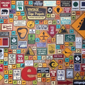 May include: A collection of vintage signs on a wooden background. The signs feature various warnings, directions, and humorous messages. The signs include text such as "Unload Here", "Grizzly Country", and "Bike Lane". The signs are in various shapes and colors.