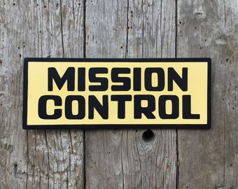 May include: A yellow sign with black text that reads "MISSION CONTROL".