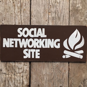 May include: A brown wooden sign with white text that reads "SOCIAL NETWORKING SITE" and a white silhouette of a campfire with flames.