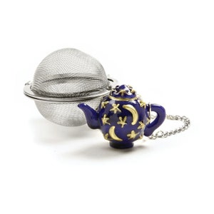 May include: A stainless steel tea infuser with a decorative blue teapot-shaped handle. The teapot is adorned with gold stars and crescent moons. A silver chain is attached to the teapot. The tea infuser is designed for steeping loose leaf tea.