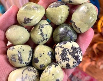 Può includere: Una collezione di pietre rotonde di colore verde-giallo e nero. Le pietre hanno un motivo maculato e sono lisce e levigate.