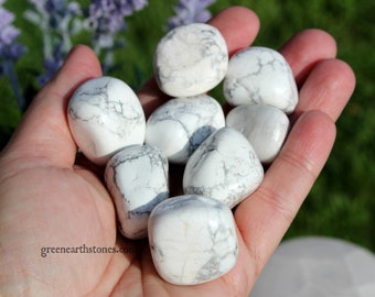May include: A hand holding a collection of white howlite tumbled stones. The stones are smooth and have a white and gray marbled pattern.