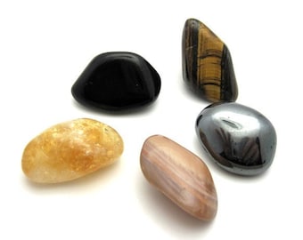 May include: Five tumbled stones in various colors and shapes, including a black stone, a brown and white striped stone, a yellow stone, a gray stone, and a brown and gold striped stone.