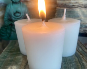 Può includere: Tre candele votive bianche, una delle quali è accesa, su una superficie di marmo verde.