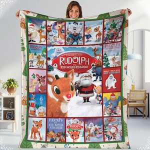 May include: A large, rectangular blanket featuring a collage of images from the animated film "Rudolph the Red-Nosed Reindeer." The blanket has a cream-colored background with green borders and images of Santa Claus, Rudolph, and other characters.