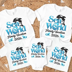 May include: White t-shirts and a onesie with the text "Sea World Family Vacation 2026". The design includes a blue and black orca and waves. The shirts are short-sleeved.