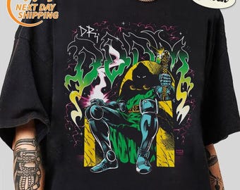 May include: A black short-sleeve t-shirt featuring a graphic print of a cloaked figure sitting on a throne. The design includes green and yellow flames, purple lightning, and the text DOOM in a stylized font. The shirt has a crew neckline.
