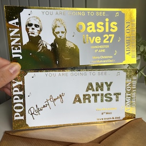May include: Two rectangular gold foil concert tickets with white backgrounds. The top ticket features the text 'YOU ARE GOING TO SEE.. oasis live 27', 'MANCHESTER 8th JUNE', 'Merry Christmas Love Mum and Dad', and 'JENNA'. The bottom ticket reads 'ANY ARTIST'.