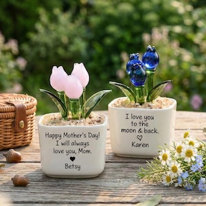 May include: Two small white square planters with glass flower sculptures. One has pink tulip-shaped flowers, the other blue. Text on the planters reads "Happy Mother's Day!" and "I love you to the moon & back."