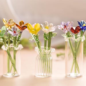 May include: Six glass flower arrangements in clear glass vases. The flowers are in various colors, including green, yellow, orange, purple, and blue.