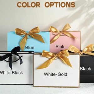 May include: Five gift bags with different colored ribbons and labels. The bags are white, blue, pink, black, and white with gold ribbon. The labels read "White-Black", "Blue", "Pink", "Black", and "White-Gold".